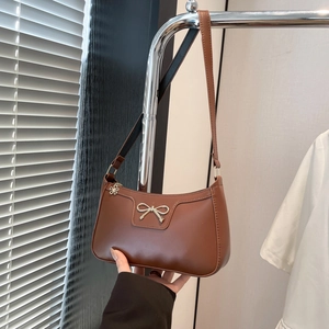 Détail du sac à bandoulière en cuir marron avec nœud doré et tirette de zip fleurie