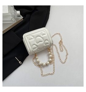 Detail of white mini bag featuring heart-shaped embossing and elegant pearl handle