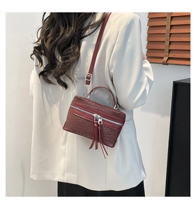 Sac bandoulière en cuir tressé bordeaux avec pompons porté par un mannequin chic