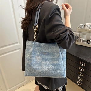 Blue denim tote bag with gold chain strap shown from a side-view angle on a model