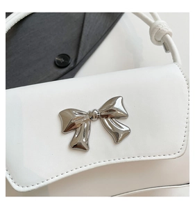Detail shot of white leather shoulder bag featuring a silver metal bow and knotted strap