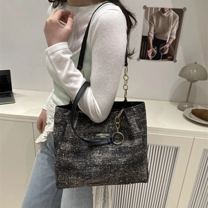 Minimalist grey tweed tote bag with black leather straps and gold chain worn by a model