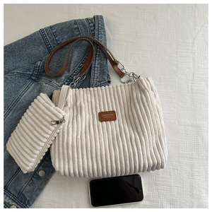 Detail of cream corduroy tote bag set with brown leather strap and chain accent