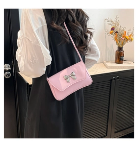 Close-up of pink crossbody bag with silver bow ornament and slim leather shoulder strap