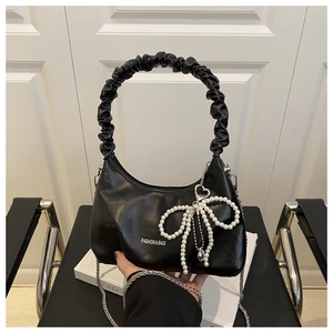 Detail of soft black cloud bag with pearl bow charm and silver chain on textured leather