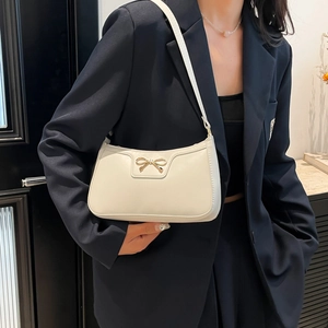 Sac baguette blanc élégant avec détail nœud doré porté sur une veste de costume