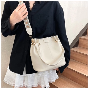 Detail of off-white bucket bag featuring ethnic embroidered wide strap and gold rivets