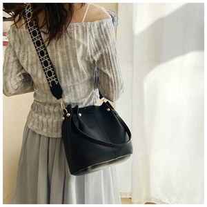 Detail of black pebbled leather bucket bag with gold bead clasp and wide woven strap