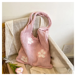 Détail d'un cabas en tricot rose orné de motifs floraux blancs sur texture tissée