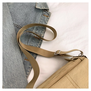Detail of khaki nylon crossbody bag showing wide woven strap and silver metal buckle