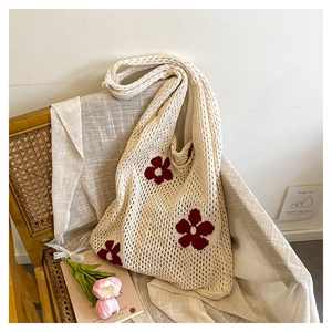Détail d'un sac cabas en crochet beige avec motifs floraux rouges sur chaise en rotin