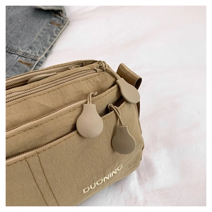Detail of khaki nylon crossbody bag showing multiple zippers and embroidered logo