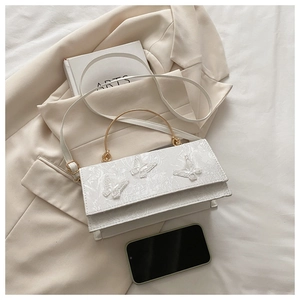 Detail of white lace shoulder bag with golden metal handle and 3D butterfly decor
