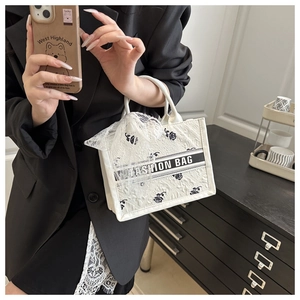 Close-up of white lace tote bag with black rose patterns and fashion bow detail