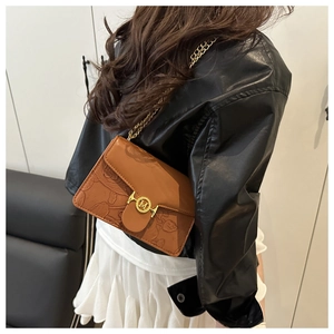 Detail of a brown embossed crossbody bag with golden chain strap and round metal buckle