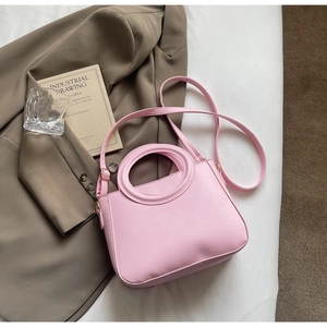 Pink minimalist handbag with round cutout handle and leather strap on a fabric background