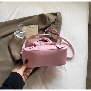 Detailed view of a pink bow handbag with PU leather texture on a white bed sheet