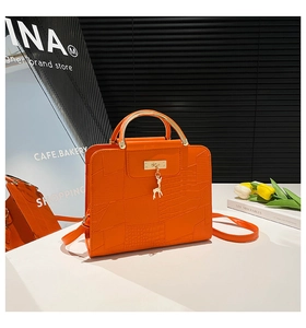 Close-up of orange crocodile pattern leather handbag with gold handle and deer charm