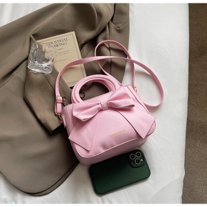 Pink bow handbag and adjustable strap shown on white cloth with lifestyle accessories