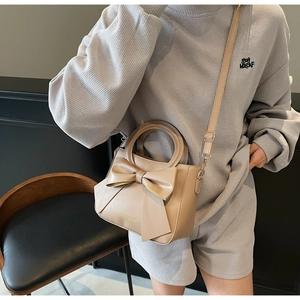 Close-up of a beige handbag with a large bow detail and hard circular handle on a model