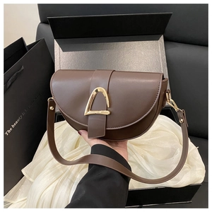 Detail of a dark brown leather saddle bag with a golden stirrup buckle in luxury packaging