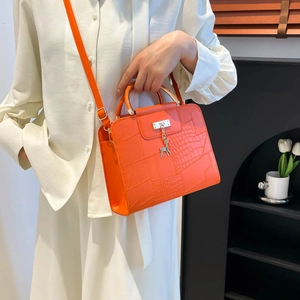Orange crocodile embossed handbag with deer pendant shown on a model for daily use
