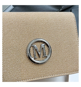 Dettaglio macro di borsa intrecciata beige e marrone con logo M in metallo argentato