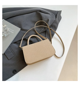 Détail du sac boîte beige texturé avec boucles dorées et anse sur un blazer gris