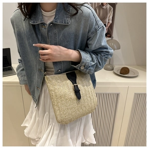 Detalle de un bolso tote de paja beige con correas de cuero negro y una hebilla dorada