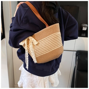 Detail of a large striped straw tote bag with white lace bow and leather straps