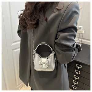 Detail of a mini silver metallic bag with bow and chain strap on a model's grey blazer