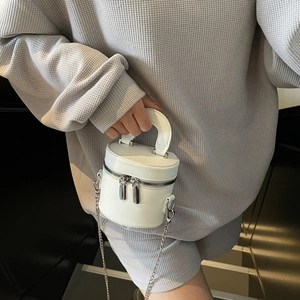 White cylindrical bucket bag with dual zippers and silver chain strap held by model