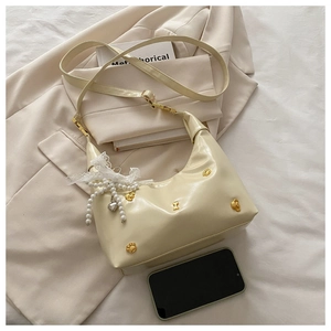 Detail of cream saddle bag with golden bear studs, lace bow and pearl charm on a blazer