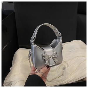 Détail du mini sac argenté avec nœud en métal et bandoulière chaîne dans une boîte cadeau