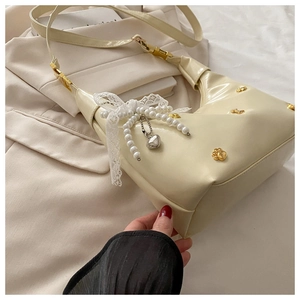 Detail of cream shoulder bag featuring pearl strap, lace bow, and cat metal ornament