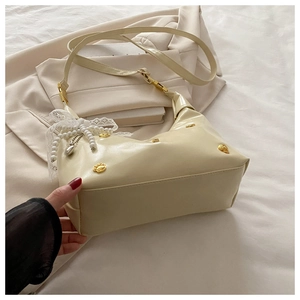 Detail of cream half-moon underarm bag with gold cat-paw charm and pearl bow decoration