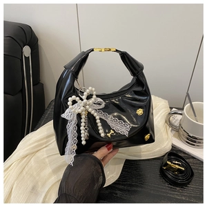 Close-up of black patent leather handbag with pearl lace bow and golden metal lock