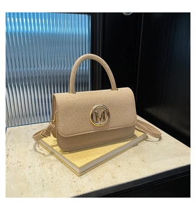 Détail du sac beige avec tissu texturé et boucle dorée en forme de lettre M