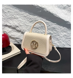 Close-up of beige woven texture handbag featuring a round gold metal M logo detail