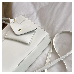 Detailed close-up of white minimalist leather bag with mini envelope pouch and embossed logo