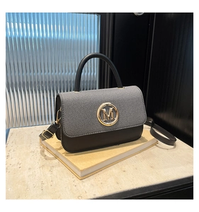 Détail du sac bandoulière élégant avec boucle logo M dorée posé sur un livre décoratif