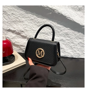 Macro detail of black pebble leather handbag with gold M logo and stitching