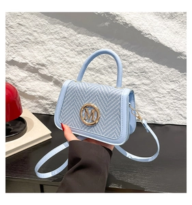 Close-up of light blue woven bag with a gold M logo and leather top handle detail