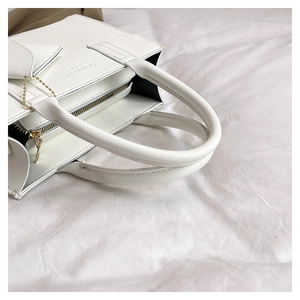 Detail view of white leather tote bag with zip closure and fashion logo embossing