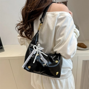 Black patent leather shoulder bag with pearl bow and gold accents on female model