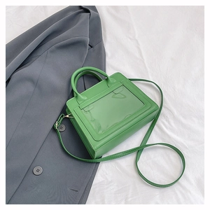 Gros plan d'un sac bandoulière vert brillant posé sur un blazer gris et tissu plissé