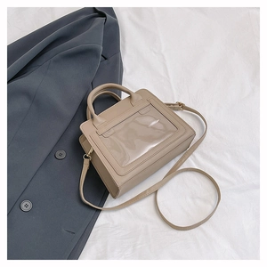 Détail du sac à main kaki avec fenêtre transparente et bandoulière sur une veste grise