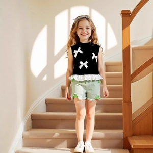 Close-up of black sleeveless top with white bows, lace hem and green denim shorts