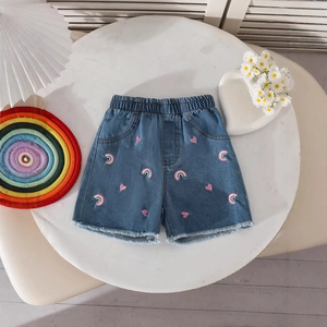 Detail of girls denim shorts featuring rainbow embroidery and frayed hem edges