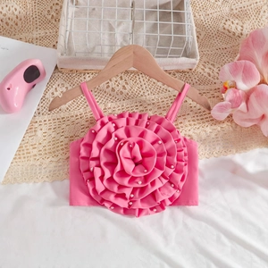 Détail d'un haut rose pour fille avec fleurs 3D et perles sur un cintre en bois
